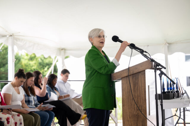 Woman with gray hair and in a green suit standing at a podium