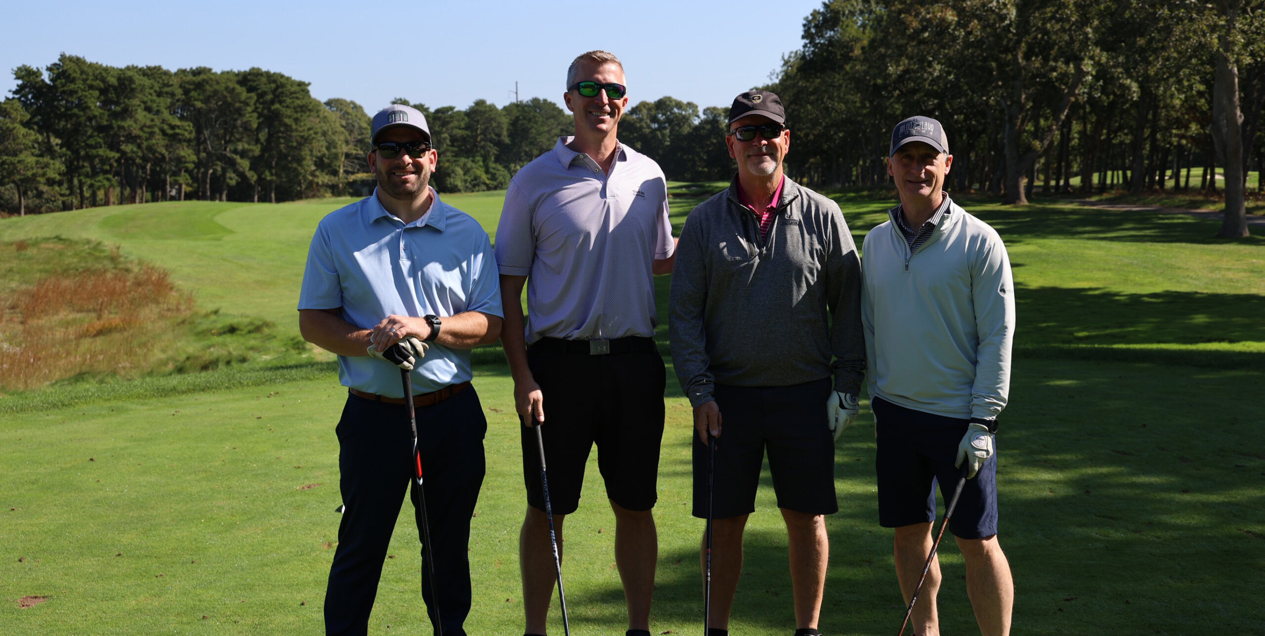 4 people standing with golf clubs on a golf course.